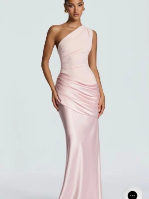 Ljusrosa satinlångklänning oneshoulder - Elegant långklänning i ljusrosa satin med oneshoulder-design och draperad midja. Klänningen har en figurnära passform och en mjukt skimrande yta som ger en lyxig känsla. Perfekt för speciella tillfällen.