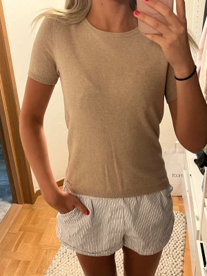 Stickad tröja - Snygg kortärmad beige stickad tröja från Lexington. Den har en liten fläck över höger bröst, men verkligne inget som syns tydligt (se bild 2). Storlek XS. Passar XS/S skulle jag tro. Nyskick.