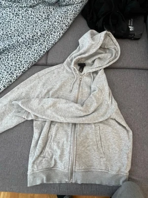 Zip Hoodie - Säljer en klassisk grå zip-hoodie från H&M. Hoodien har dragkedja framtill, två fickor och justerbar huva med snören. Tillverkad i mjukt sweatshirtmaterial, perfekt för en avslappnad stil. Riktigt bra kvalité, perfekt för en tonåring. Ingenting är fel med den, passar mig inte längre. 