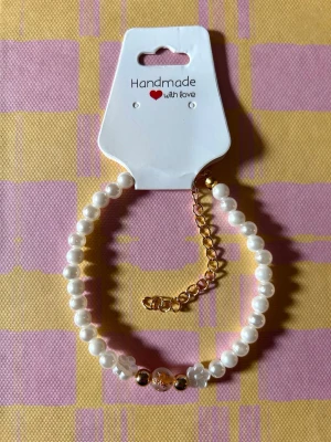 Pärlarmband med gulddetaljer - Stilrent armband med vita pärlor och guldfärgade detaljer. Justerbar kedja i guldton och små dekorativa pärlor i mitten. Perfekt accessoar för att lyfta din outfit.