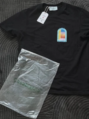 Svart t-shirt från Casablanca - Svart t-shirt från Casablanca med färgglatt grafiskt tryck fram och stort tryck på ryggen. Klassisk passform och rund hals. Tillverkad i mjuk bomull och perfekt för en trendig streetwear-look.