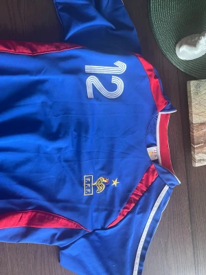 Frankrike fotbollströja Henry #12 - Blå fotbollströja från Frankrikes landslag med nummer 12 och namnet Henry på ryggen. Tröjan har röda och vita detaljer samt FFF-emblem med stjärna på bröstet. Perfekt för fotbollsfans som vill visa sitt stöd för landslaget.