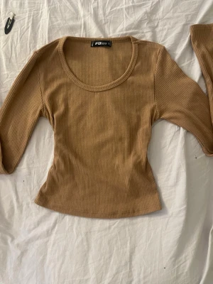 Beige ribbad topp från FB Sister - Snygg beige ribbad topp från FB Sister med rund halsringning och lång ärm. Toppen har en figurnära passform och är perfekt att styla med jeans eller kjol. Enkel och stilren design som passar till många olika looks.