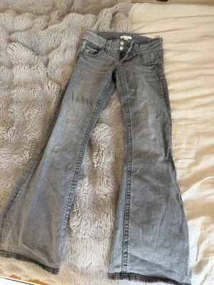 Grå bootcut jeans med låg midja - Snygga grå jeans med bootcut och låg midja. Klassisk femficksmodell med dragkedja och dubbla knappar framtill. Tillverkade i mjukt denimtyg. Jättefina jeans och bra kvalité, 🩶
