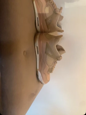 Nike Jordan 4 - Snygga Nike Air Jordan sneakers i beige och rosa med vita detaljer. Skorna har klassisk meshpanel på sidorna, synlig luftdämpning i sulan och cool retrodesign. Perfekta för dig som gillar streetwear och vill sticka ut med stilrena färger och ikonisk siluett.