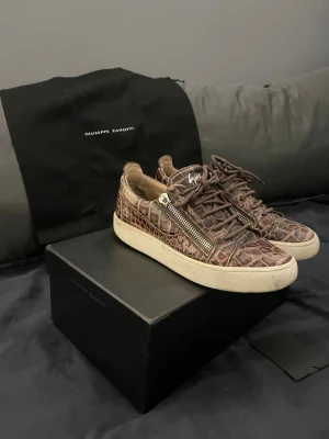 Bruna Giuseppe Zanotti skor - Säljer nu dessa unika bruna skor från giuseppe zanotti men ett crocodile liknade läder mönster. | De är använda och det finns några skavanker. En av de är att en av sakerna som man drar i dragkedjan med har lossnat på en sidan av en av skorna. Men det är inget som påverkar användningen av skorna. Du kan se vad jag menar på de sista bilderna i annonsen. Och delen som lossnat följer självfallet med. Skorna är rätt så nötta på hälen kan vara bra att veta. | Skriv i fall du har några frågor.