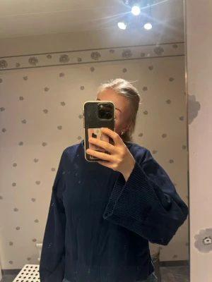 Mörkblå stickad tröja med vida ärmar - Mysig mörkblå stickad tröja med oversized passform och extra vida ärmar. Tröjan har ribbstickade muddar och en rak, avslappnad siluett. Perfekt att slänga på sig över ett par jeans för en chill look.