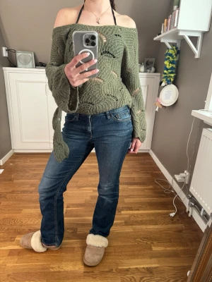 Olivgrön off shoulder stickad tröja - Säljer en olivgrön stickad tröja med off shoulder-modell och vida ärmar. Tröjan har ett coolt hålmönster och knytband i sidan för extra detalj. Perfekt för dig som gillar en avslappnad men trendig stil.
