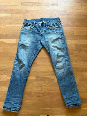 Blå slitna jeans från Polo Ralph Lauren - Säljer ett par blå jeans från Polo Ralph Lauren med snygga slitningar och klassisk femficksmodell. Jeansen har raka ben och är tillverkade i bomullsdenim. Perfekta för en avslappnad och trendig look.