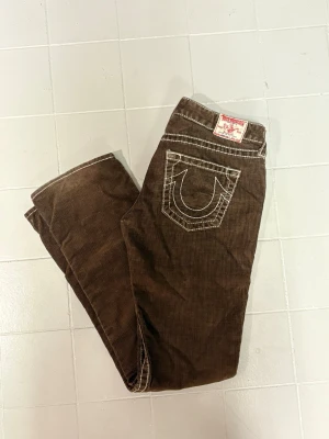 Bruna manchesterbyxor True Religion - Snygga bruna manchesterbyxor från True Religion med klassisk vit kontrastsöm och ikonisk bakficka. Byxorna har rak passform (liite bootcut) och är tillverkade i mjuk manchester