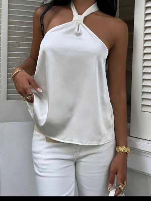 Vit halterneck linnetopp i satin - Snygg vit halterneck linnetopp i glansigt satinmaterial. Toppen har en lös passform och knyts elegant i nacken. Perfekt för dig som vill ha en stilren och trendig look med en touch av lyx.
