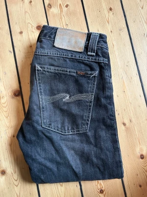 Svarta jeans från Nudie Jeans - Säljer ett par svarta jeans från Nudie Jeans med klassisk femficksmodell och vita kontrastsömmar på bakfickorna. Jeansen har rak passform och är tillverkade i denim med en snygg tvätt. Perfekta för dig som gillar stilrena och tidlösa jeans. Pris kan diskuteras och det är bara att fråga på! 