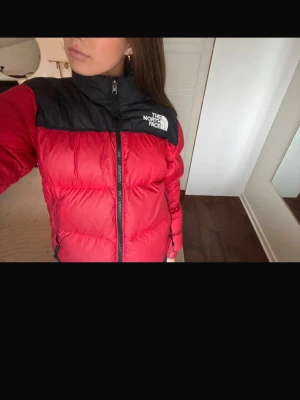 Röd pufferjacka från The North Face - Säljer en röd och svart pufferjacka från The North Face. Jackan har en klassisk boxig passform och logga på bröstet. Perfekt för kalla vinterdagar. Den har en fläck på baksidan upp mot nacken. 