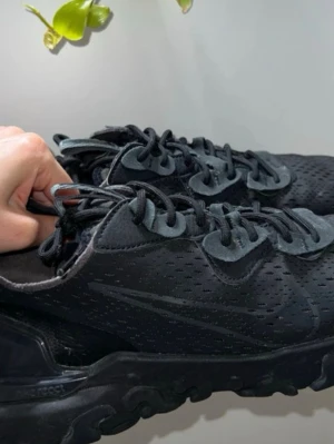 Svarta Nike React Element 55 sneakers - Snygga helsvarta Nike React Element 55 sneakers med perforerad ovandel och klassisk Nike-logga på sidan. Skorna har en chunky sula med React-dämpning och svarta skosnören. Perfekta för dig som gillar en stilren och sportig look.