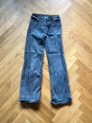 Grå raka jeans med hög midja - Säljer ett par grå jeans med raka ben och hög midja. Klassisk femficksmodell med dragkedja och knapp framtill. Jeansen har bälteshällor och är tillverkade i ett slitstarkt denimtyg. Perfekta för en avslappnad och trendig look.
