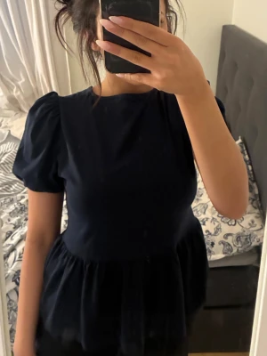 Svart topp med puffärm och rosett - Snygg svart topp med puffärmar och rund halsringning. Toppen har en peplumliknande volang nertill och öppen rygg med tre dekorativa rosetter. ALDRIG ANVÄNT PLAGGET✨✨