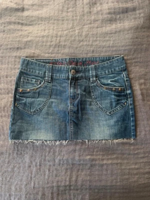 Blå jeanskjol från Esprit - Säljer en blå jeanskjol från Esprit med fransig kant. Kjolen har låg midja och en snygg passform!