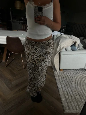 Leopardmönstrad långkjol - Säljer en snygg långkjol med leopardmönster i beige, svart och bruna toner. Kjolen har en rak passform och är tillverkad i ett mjukt, följsamt material som ger en skön känsla. Perfekt för dig som vill sticka ut med ett trendigt djurmönster.
