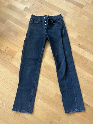 Svarta raka jeans från Zara - Snygga svarta jeans från Zara med raka ben och hög midja. Jeansen har klassisk femficksdesign och knäppning med knappar framtill.
