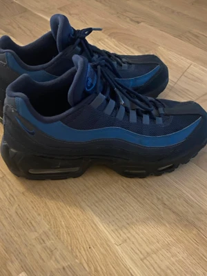 Nike Air Max - Nike Air Max 95 sneakers i mörkblått och svart med reflekterande detaljer. Skorna har en chunky sula med synliga Air-enheter, mesh och syntetmaterial på ovandelen samt klassisk snörning. Perfekta för dig som gillar streetwear och sportig stil.