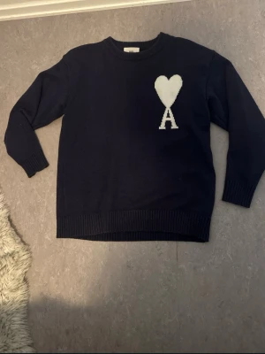Mörkblå stickad tröja från Ami - Snygg mörkblå stickad tröja från Ami Alexandre Mattiussi. Tröjan har rund halsringning, långa ärmar och ribbade muddar vid ärmslut och nederkant. Tillverkad i Portugal med högkvalitativt material för en stilren look. Pris kan diskuteras 