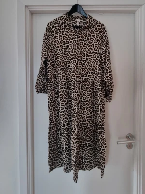 Leopardmönstrad långklänning H&M - Säljer en snygg långklänning med leopardmönster i beige och svart. Klänningen har lång ärm och en lös passform som ger en avslappnad look. Materialet känns mjukt och följsamt, 100% viskos. 