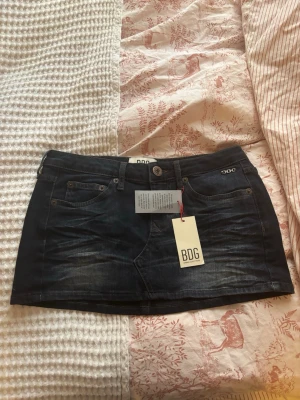Mörk jeanskjol från BDG-Urban Outfiters - Snygg mörkblå jeanskjol från BDG med klassisk femficksdesign och knappstängning fram. Kjolen  har en cool tvättad look samt BDG-logga på bakfickan. 