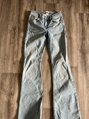 Ljusblå bootcut jeans Gina tricot  - Säljer ett par ljusblå bootcut jeans från Gina tricot med klassisk femficksdesign och läderpatch bak i midjan. Jeansen har en avslappnad passform och är tillverkade i slitstark denim. Perfekta för en casual och trendig look.