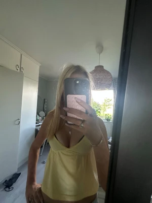 Gul tröja med v-ringning - Säljer en söt gul body med djup v-ringning och tunna axelband. Modellen är figurnära upptill och har en lösare passform nedtill. Perfekt för dig som gillar en enkel men stilren look. Materialet känns mjukt och bekvämt mot huden.