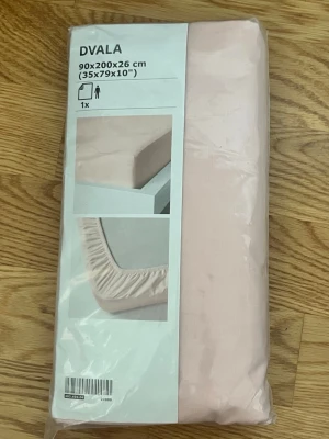 Ljusrosa dra-på-lakan DVALA 90x200 - Ljusrosa dra-på-lakan från IKEA:s serie DVALA i storlek 90x200x26 cm. Tillverkat i mjukt bomullstyg och har resår runt kanten för att sitta bra på madrassen. Perfekt för enkelsäng och ger en fräsch känsla till sovrummet.