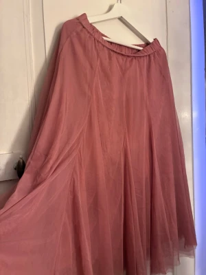 Rosa tyllkjol från Newbie - Säljer en fluffig och romantisk rosa tyllkjol från Newbie. Kjolen har resår i midjan och flera lager tunt tyg som ger ett fint fall. Perfekt för dig som vill ha en söt och trendig look med extra volym.