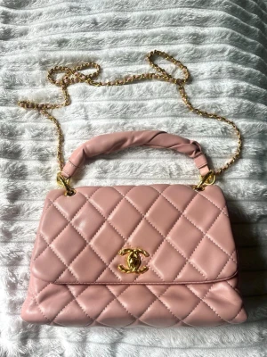 Rosa quiltad handväska  - Supersnygg rosa handväska från i quiltat läder med guldfärgade detaljer. Väskan har både ett vadderat handtag och en lång kedjerem i guld, samt den klassiska loggan framtill. Perfekt för dig som vill ha en lyxig och trendig accessoar. 🌸