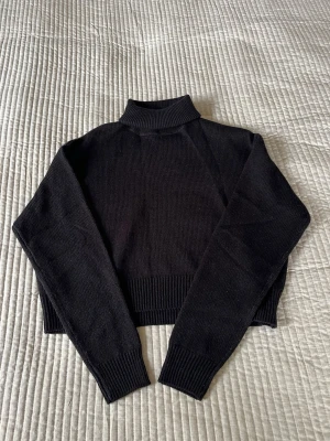 Svart croppad stickad tröja Divided - Säljer en svart croppad stickad tröja från H&M Divided. Tröjan har hög krage, långa ärmar och bred ribbstickad mudd vid ärmslut och nederkant. Perfekt till höst och vinter när det börjar bli lite kallare och för en stilren look.
