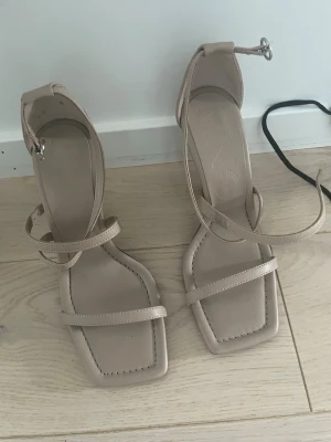 Beige pumps  - Säljer ett par trendiga beige pumps med hög smal klack och fyrkantig tå. Skorna har tunna remmar över foten och runt ankeln som ger en stilren look. Tillverkade i konstläder med minimalistisk design, perfekta för dig som gillar modern stil. Storlek 36, utmärkt skick! Hör av er💕