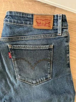 Levi's blå bootcut jeans - Klassiska blå jeans från Levi's med bootcut-modell och fem fickor. Jeansen har den ikoniska röda Levi's-lappen på bakfickan och patch i läder bak i midjan. Tillverkade i slitstark denim med snygga slitningar och kontrastsömmar. Lite slitage längst nere på kanterna (bild 4) men är annars i bra skick!💗