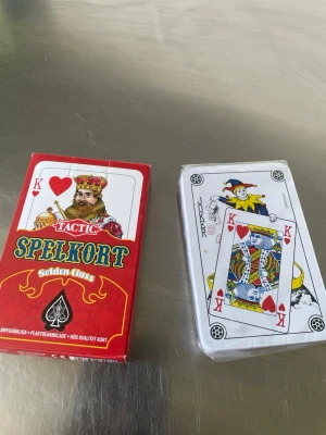 Spelkort Tactic Golden Classic - Kortlek från Tactic i serien Golden Classic. Förpackningen är röd med gulddetaljer och innehåller klassiska spelkort med plastlaminerad yta. Perfekt för poker, patiens eller andra kortspel. Kortleken har traditionella färger och motiv.