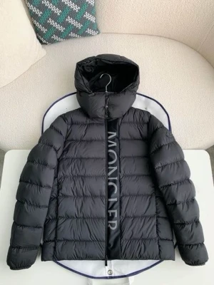 Svart dunjacka med huva från Moncler - Snygg svart dunjacka från Moncler med stor logga längs dragkedjan. Jackan har en puffig design, huva och raka ärmar. Perfekt för kalla vinterdagar och riktigt trendig stil.