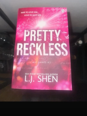 Pretty Reckless av L.J. Shen - En skönlitterär bok med titeln 'Pretty Reckless' av L.J. Shen. Omslaget är rosa och vitt med ett sprakande ljusmönster och tydlig text. Boken är i pocketformat och tillhör serien All Saints. Perfekt för dig som gillar romantik och drama.