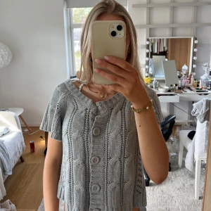 Grå stickad kofta med knappar - Säljer en grå stickad kofta med korta ärmar och stora knappar framtill. Koftan har en ribbad struktur och kan bäras offshoulder.