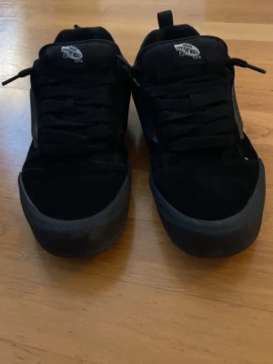 Svarta Vans knu Skool sneakers - Säljer ett par helsvarta Vans Old Skool sneakers med klassisk låg siluett. Skorna har mockadetaljer, textilpartier och den ikoniska Vans-sidan i svart. Tjock sula och 'Off The Wall'-logga på plösen och hälen. Perfekta för en clean och stilren look.