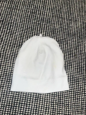 Vit mössa från H&M i ekologisk bomull - En enkel och stilren vit mössa från H&M, tillverkad i mjuk ekologisk bomull. Mössan har en klassisk form utan detaljer eller mönster, perfekt för en clean och minimalistisk look.