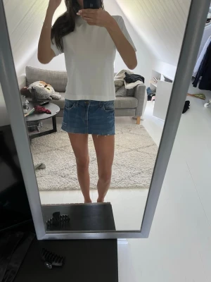 Blå jeanskjol i klassisk modell - Säljer en blå jeanskjol i kort modell med klassisk femficksdesign och knapp- samt dragkedjestängning framtill. Kjolen har en rak passform och är perfekt för en avslappnad stil. Passar till många olika toppar och sneakers.