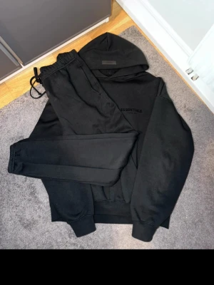 Essentials tracksuit - Essentials Tracksuit Set – Svart 🖤 Snygg och bekväm hoodie + mjukisbyxor från Essentials. Använd få gånger och i mycket fint skick utan synliga defekter. Perfekt för både vardag och chill. Storlek M äkthet kan bevisas