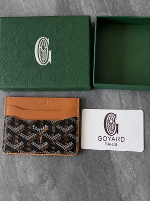 Goy4rd - Snygg korthållare från Goy4rd i brunt och svart med klassiskt mönster och detaljer i läder. Kompakt och smidig design med flera fack för kort. Perfekt accessoar för dig som vill ha något både stilrent och exklusivt. Levereras med originalask och dustbag.