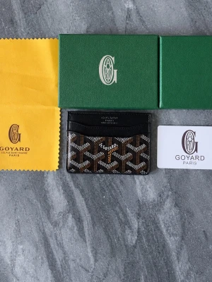  Goy4rd - Snyggt svart kortfodral från Goy4rd med det klassiska mönstret i vitt, brunt och grått. Tillverkat i canvas och läder med flera fack för kort. Perfekt accessoar för dig som vill ha något både stilrent och exklusivt.