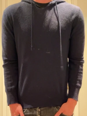 Softgoat cashmere - Mörkblå hoodie med huva och dragsnören. Tillverkad i ett mjukt, stickat material som ger en avslappnad look. Den har ganska många defekter därav priset. Men går att lösa hos butik för 500kr ungefär