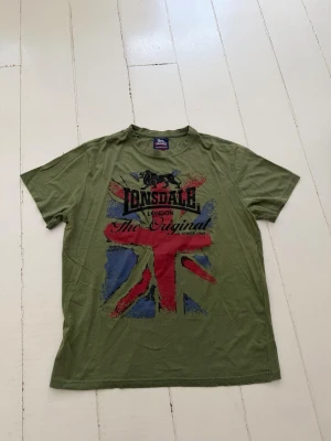 Grön Lonsdale t-shirt med tryck - Säljer en grön t-shirt från Lonsdale med stort tryck av Union Jack-flaggan och texten 'The Original' på framsidan. Synligt använd men ger en snygg stil. Stl L och gjord av bomull.
