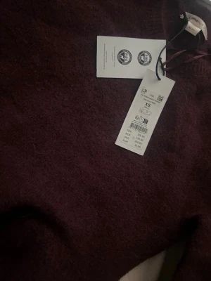 Mörklila stickad tröja från Gina Tricot - Mysig mörklila stickad tröja från ARKET i storlek XS. Tröjan har en enkel, klassisk design med rund halsringning och långa ärmar. Materialet är mjukt och fluffigt, perfekt för kyliga dagar.