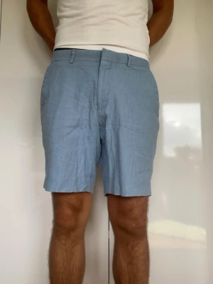 Ljusblåa linneshorts  - Ljusblåa shorts i linne och bomulls blandning från märket ASOS. Strl 32. Det finns en väldigt liten fläck vid gylfen (se bild 4, den svarta pricken). Modellen är 178 cm och väger 77 kg. Hör gärna av dig vid frågor!