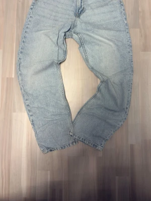 Ljusblå baggy jeans i vintage-stil - Säljer ett par ljusblå baggy jeans med lös passform och hög midja. Jeansen har klassisk femficksdesign och är tillverkade i denim. Perfekta för en avslappnad och trendig look.